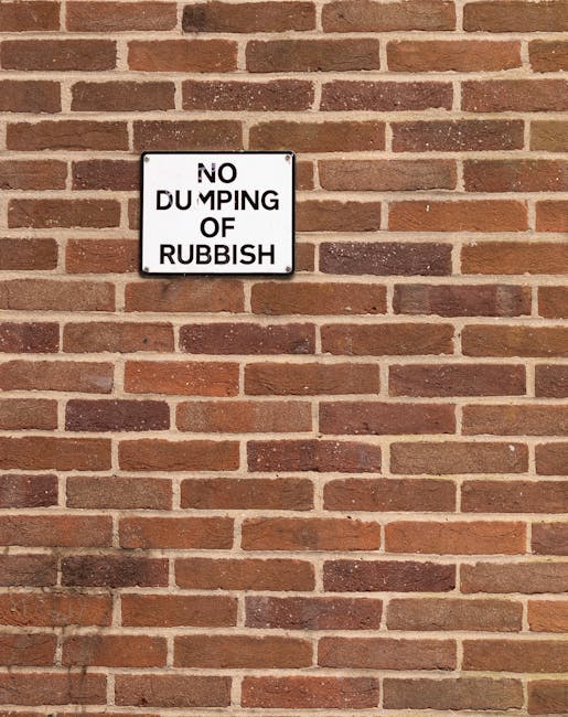 A close-up view of a red brick wall with a white rectangular sign mounted on it. The sign displays the text 'NO DUMPING OF RUBBISH' in black capital letters, with some characters slightly obscured or